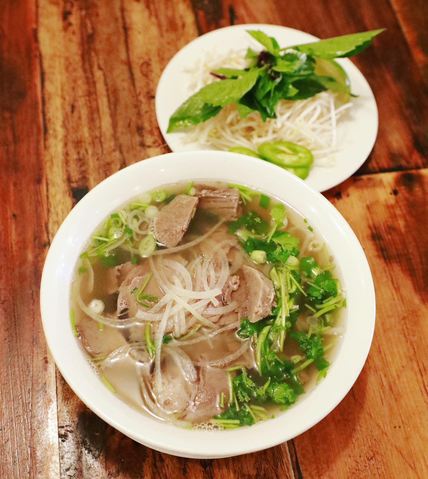 Steaming bowl of authentic Hue-style beef pho with fresh rice noodles, tender beef slices, vibrant herbs, and aromatic broth at La Ca Bar in Tacoma, Washington