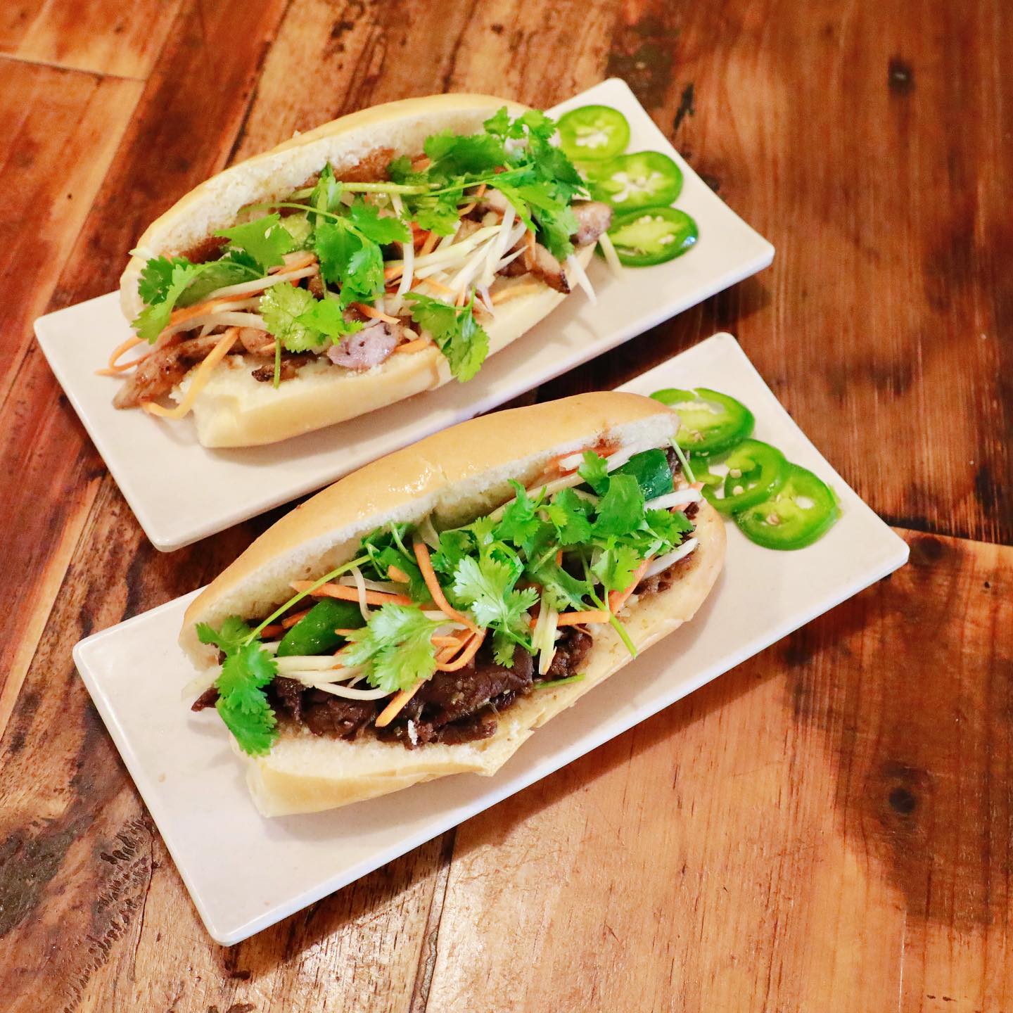 Two authentic Vietnamese bánh mì sandwiches with grilled pork and chicken, fresh cilantro, pickled vegetables, jalapeños on crispy French baguettes at La Ca Bar, Tacoma