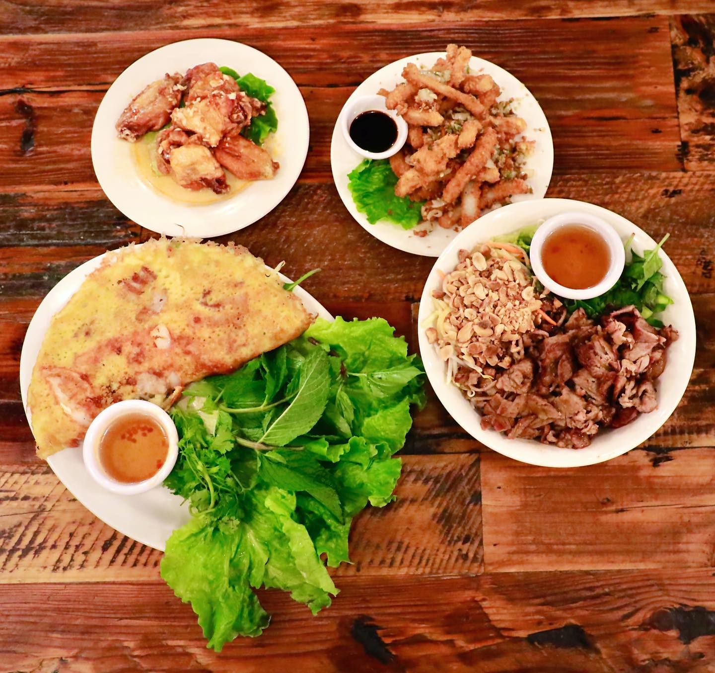 Authentic Vietnamese cuisine spread featuring bánh xèo crepe, vermicelli bowl with grilled pork, salt and pepper squid, fish sauce wings, and fresh herbs at La Ca Restaurant, Tacoma